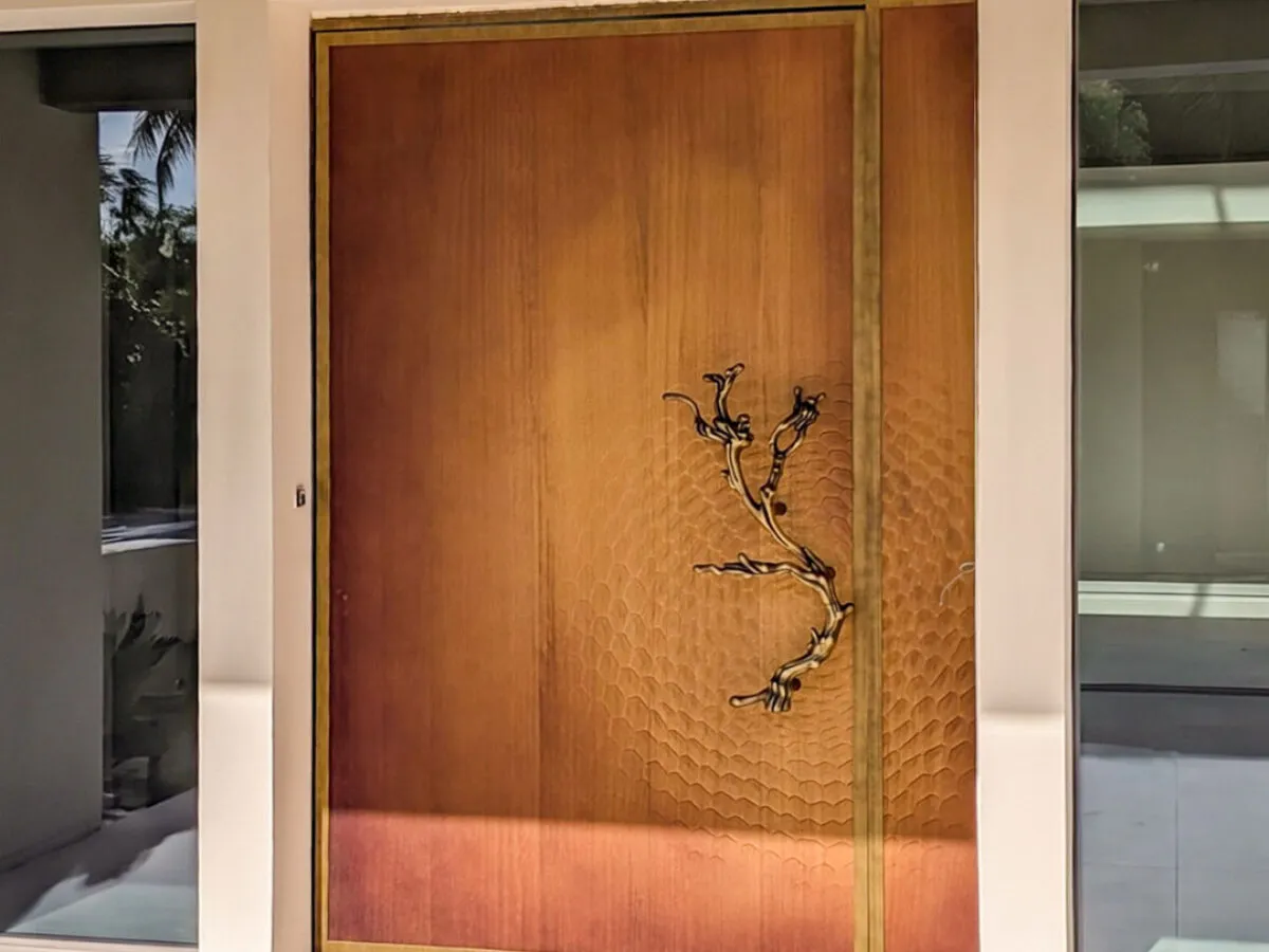 Porta d'ingresso su misura con apertura pivot, pannello in legno fresato a nido d'ape, cornice OxyBrass e maniglia scultorea a ramo, Metalbril
