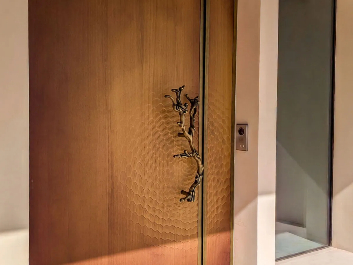 Porta d'ingresso su misura con apertura pivot, pannello fresato a nido d'ape, cornice OxyBrass e maniglia scultorea a ramo, realizzata da Metalbril